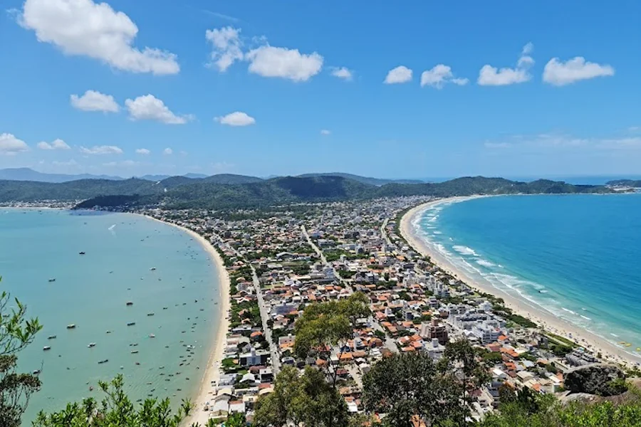 Vista panorâmica de Bombinhas, capturada do Morro do Macaco, mostrando praias de águas cristalinas, casas e montanhas ao fundo, um dos destinos mais belos de Santa Catarina.