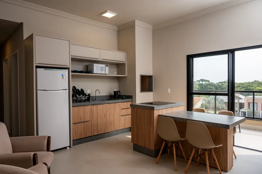 Cozinha da pousada, equipada com geladeira, micro-ondas e utensílios modernos, além de uma ilha central com cadeiras, perfeita para refeições rápidas ou momentos em família.