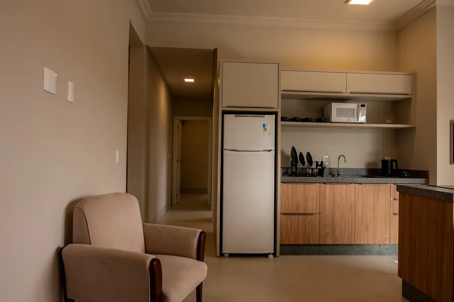 Cozinha da pousada, equipada com geladeira, micro-ondas e utensílios modernos, além de uma ilha central com cadeiras, perfeita para refeições rápidas ou momentos em família.