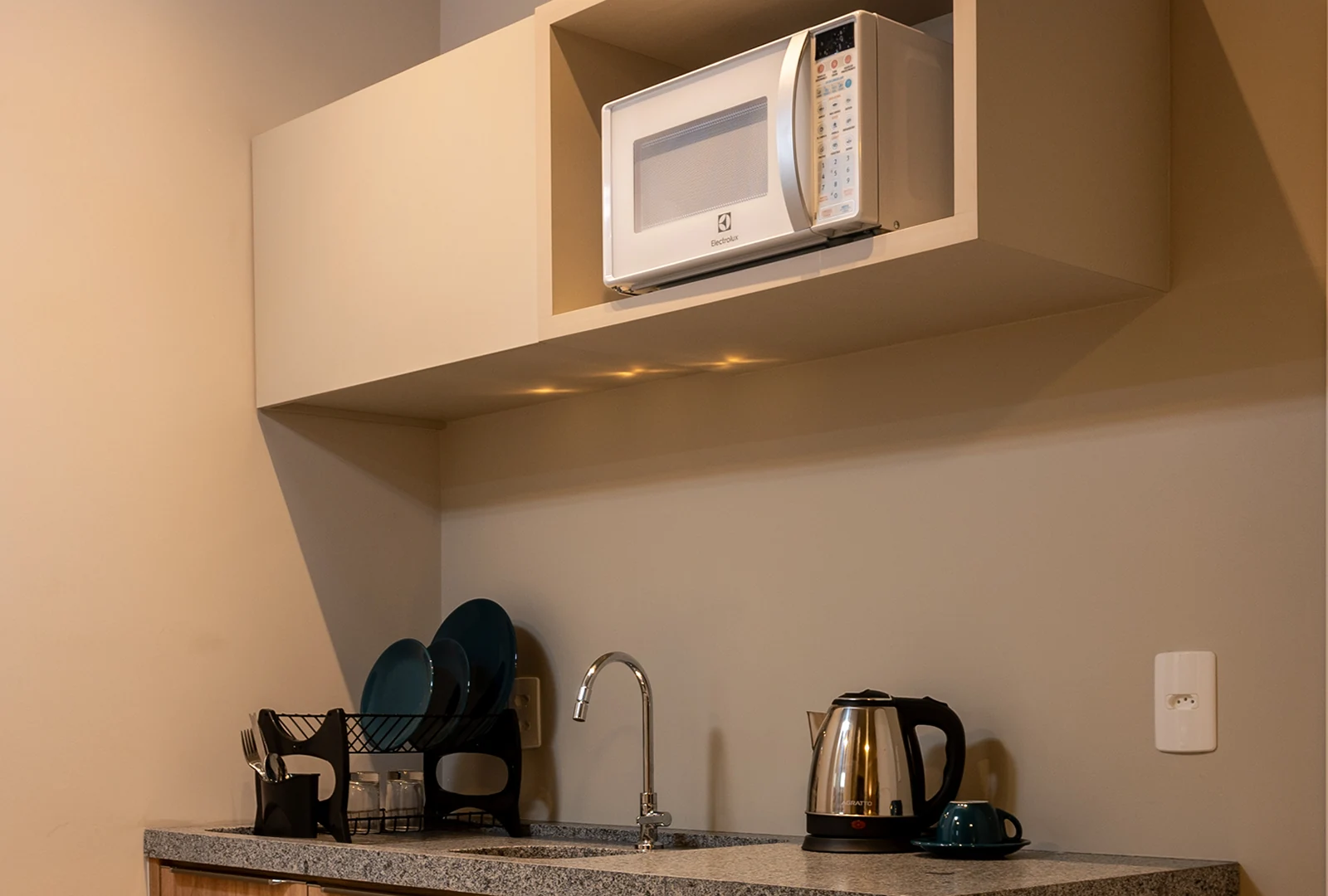 Cozinha equipada do quarto da Pousada Caminho do Bosque, com micro-ondas, chaleira elétrica, utensílios básicos e bancada moderna para maior praticidade.