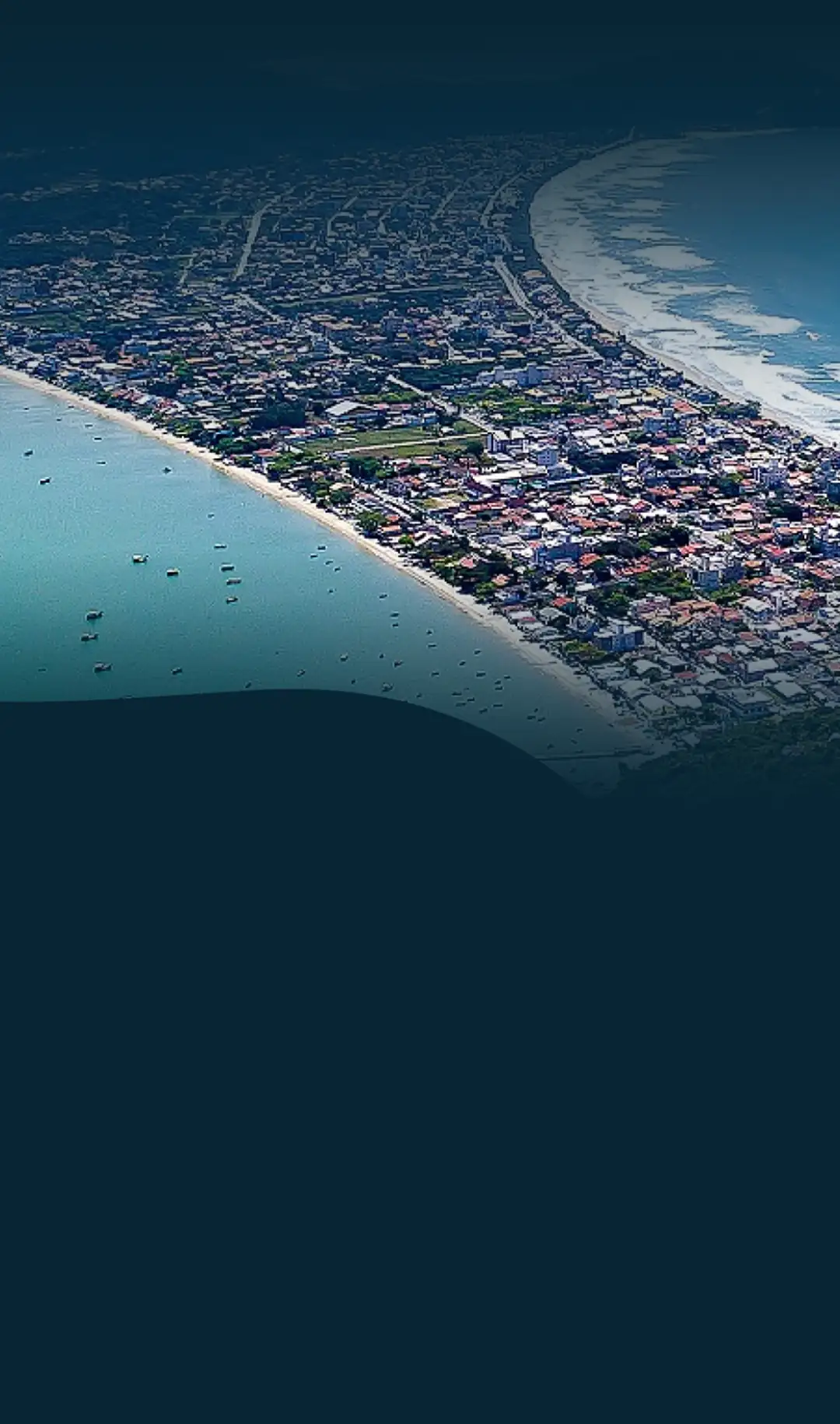 Vista aérea de Bombinhas, Santa Catarina, mostrando a praia de Canto Grande e a região montanhosa ao redor, com águas azuis e vegetação exuberante ao fundo.