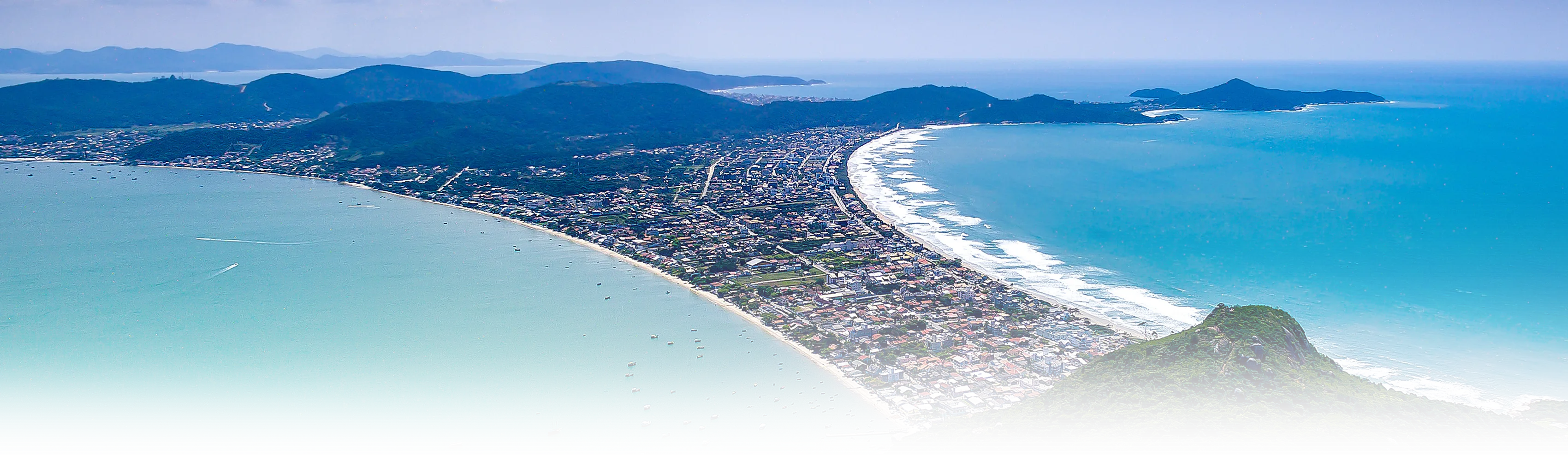 Vista aérea de Bombinhas, Santa Catarina, mostrando a praia de Canto Grande e a região montanhosa ao redor, com águas azuis e vegetação exuberante ao fundo.