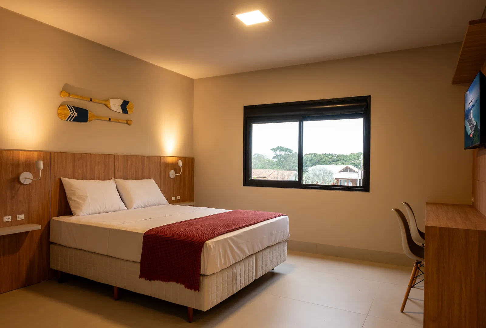 Quarto de luxo na Pousada Caminho do Bosque, com cama box queen size, decoração elegante com remos estilizados na parede e ampla janela com vista externa.