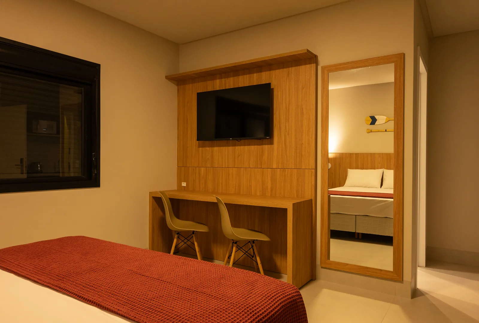Espaço funcional no quarto da Pousada Caminho do Bosque, com bancada de trabalho, espelho de corpo inteiro e TV de tela plana integrada ao ambiente.